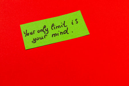 A bright green note with a motivational quote is placed on a vivid red background. The text encourages self-belief and limits formed by oneâs own mind.の写真素材