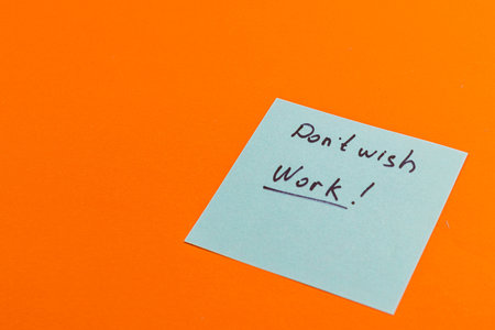 A handwritten note on a light blue sticky paper conveys a humorous sentiment about not wanting to work. The note is prominently displayed against a vibrant orange background.の写真素材