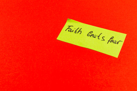Bright red background features a sticky note with the encouraging phrase about faith overcoming fear. The simplicity of the design highlights the importance of positive thinking.の写真素材