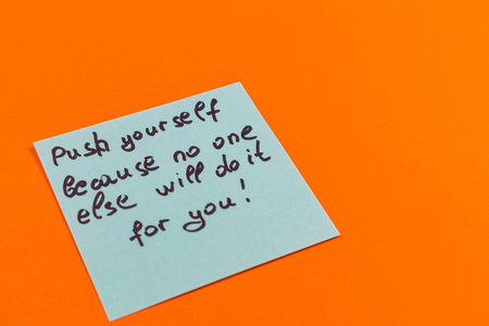 A handwritten note on a vibrant orange background reminds individuals to push themselves and strive for personal growth. The note emphasizes self-reliance in achieving goals.の写真素材