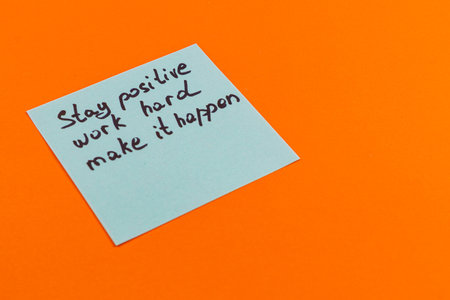 A handwritten note featuring the phrases Stay positive, work hard, make it happen is placed against a bright orange background, promoting a message of determination and optimism.の写真素材