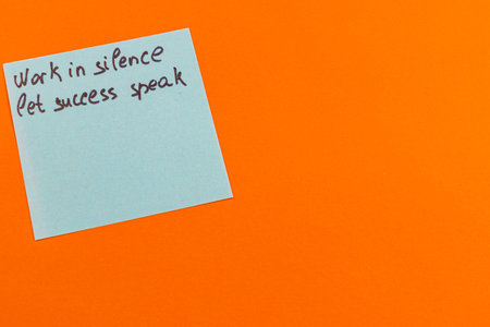 A handwritten note displays an inspirational quote on a vibrant orange surface. The saying encourages working quietly while allowing achievements to showcase one's success.の写真素材