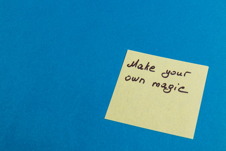 A simple sticky note featuring the handwritten phrase Make your own magic rests on a vibrant blue surface. This motivational reminder encourages creativity and personal empowerment.の写真素材