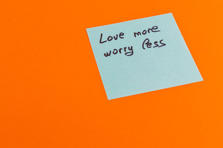 A motivational reminder encourages embracing love and reducing worries. The note features handwritten text in a casual style, set against a vibrant orange backdrop, creating a lively atmosphere.の写真素材