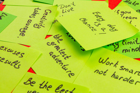Bright yellow sticky notes filled with motivational phrases cover a red surface. Phrases inspire creativity, courage, and the idea of living without limits in daily life.の写真素材