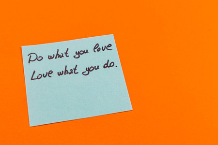 A handwritten note on a blue sticky paper displays motivational phrases about pursuing passions and dedication. The note rests against a vibrant orange background.の写真素材