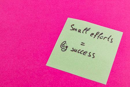 A green sticky note displays an inspiring quote emphasizing the importance of small efforts for achieving significant success. The vibrant pink background creates a striking contrast.の写真素材