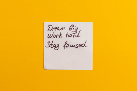A vibrant yellow backdrop features a handwritten note with motivational phrases. The message encourages perseverance and ambition, making it a perfect source of inspiration.の写真素材