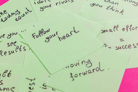 A collection of handwritten motivational notes lies on a bright pink background. Each card contains uplifting phrases encouraging perseverance, introspection, and self-belief.の写真素材