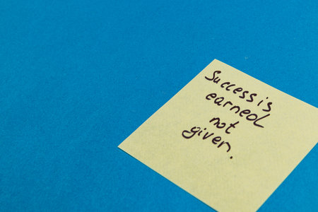 A yellow sticky note with a motivational quote is placed on a vibrant blue surface. The phrase emphasizes that success is something earned through effort, not a free gift.の写真素材