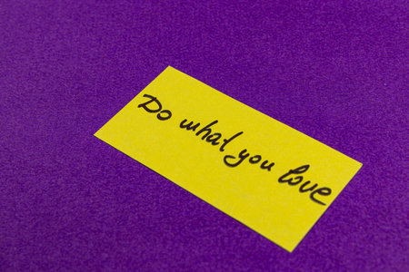 A bright yellow note with an inspiring message sits against a rich purple background, encouraging individuals to pursue their passions and love what they do in life.の写真素材