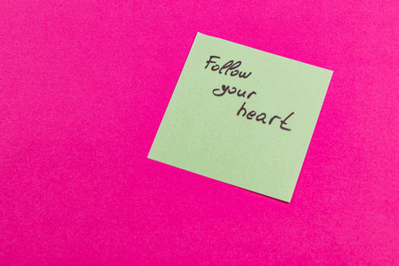 A handwritten note on a light green sticky pad displays the phrase Follow your heart. It is placed against a bright pink background, adding a pop of color and inspiration.の写真素材