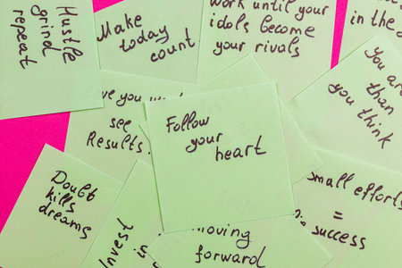A collection of handwritten motivational notes in bright green, scattered atop a vibrant pink surface, promoting positivity and focus on personal goals and achievements.の写真素材