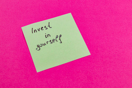 A simple sticky note is placed on a vibrant pink background, featuring the phrase Invest in yourself. This message serves as a reminder to prioritize personal development.の写真素材