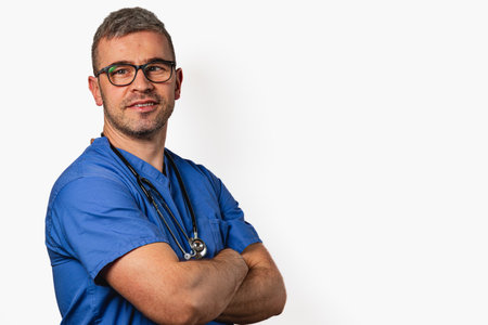 A medical professional with glasses and a stethoscope stands with arms crossed, showcasing confidence in a clinical setting. The background is minimalistic, emphasizing the subject.の写真素材