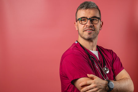 A healthcare worker dressed in vibrant scrubs and wearing a stethoscope smiles while standing against a colorful backdrop. This setting emphasizes professionalism and approachability.の写真素材