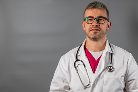 A male healthcare provider wearing glasses and a lab coat stands confidently with a stethoscope around his neck. He appears ready to engage with patients in a clinical environment.の写真素材