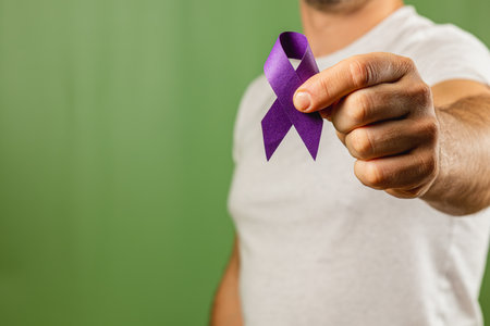 A man wearing a white shirt stands against a green background while holding a purple ribbon. This gesture symbolizes support and awareness for various causes related to health and social issues.の写真素材