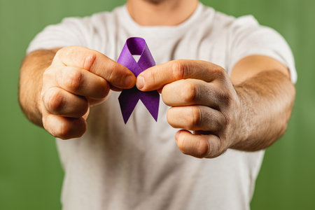 A man is holding a purple ribbon with both hands, symbolizing awareness. He is wearing a plain white shirt against a green background, promoting a cause of significance.の写真素材