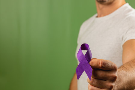 Individual displays a purple ribbon, symbolizing awareness for various causes. The person wears a plain white shirt and stands in front of a solid green background.の写真素材