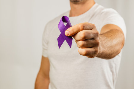 A man in a white shirt stands against a neutral background, proudly displaying a purple ribbon in his right hand to promote support and awareness for various causes.の写真素材