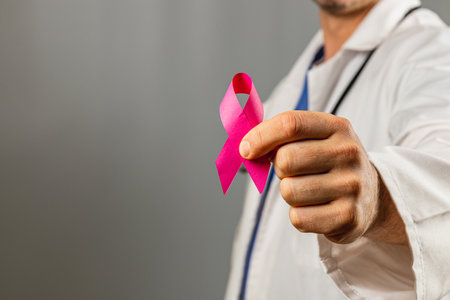 A doctor in a white coat holds a pink ribbon to promote breast cancer awareness. The setting emphasizes the importance of health education and community support in October.の写真素材