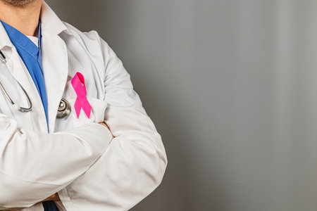 A medical professional stands with arms crossed, showcasing a pink ribbon pinned to their coat. This symbolizes support for breast cancer awareness and prevention efforts.の写真素材