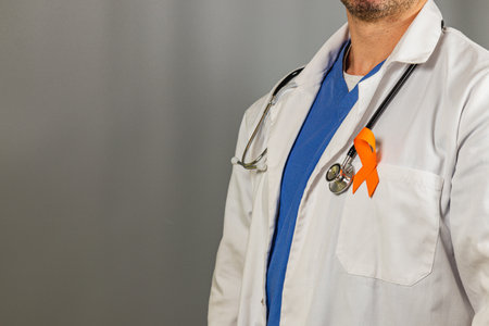 A healthcare worker wears a white lab coat over blue scrubs, displaying an orange ribbon on their lapel to promote awareness for a health initiative.の写真素材