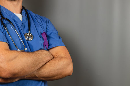 A healthcare worker in scrubs crosses arms confidently, wearing a stethoscope around the neck. A purple ribbon accentuates the uniform, symbolizing awareness for a health cause.の写真素材