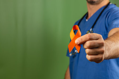 A healthcare worker in scrubs presents a vibrant orange and yellow ribbon, symbolizing support and awareness for a health cause. The event takes place against a simple green background.の写真素材