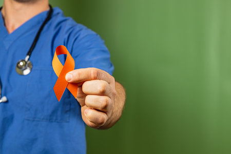 Medical professional wears scrubs and holds an orange awareness ribbon, emphasizing the importance of health campaigns and community support for various causes.の写真素材