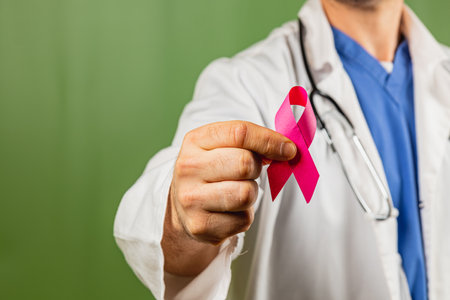 A healthcare worker in a white coat and blue scrubs displays a pink ribbon to promote breast cancer awareness, symbolizing hope and support for those affected.の写真素材