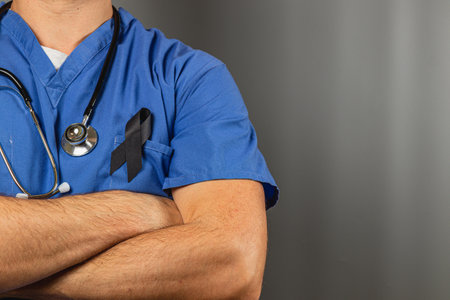 A healthcare worker in blue scrubs stands with arms crossed, wearing a black ribbon. This image symbolizes their commitment to care amidst difficulties in the medical field.の写真素材