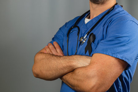 A healthcare worker stands confidently with crossed arms, wearing blue scrubs and a stethoscope. A black ribbon on the scrubs symbolizes awareness for an important cause.の写真素材