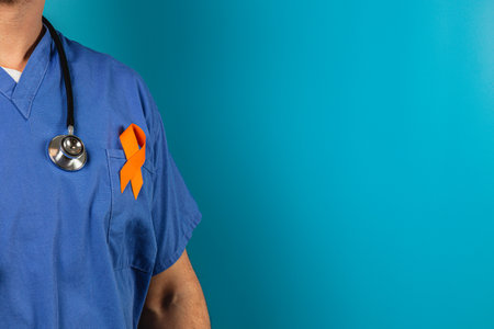 A medical professional in blue scrubs stands against a turquoise background, displaying an orange awareness ribbon on their attire, highlighting a cause of health awareness.の写真素材