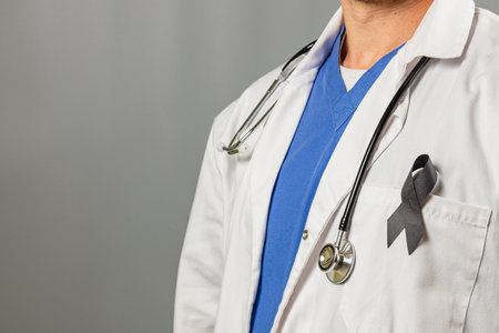A healthcare worker is wearing a white coat and blue scrubs with a stethoscope around their neck. A black ribbon is displayed as a symbol of support and awareness for an important cause.の写真素材