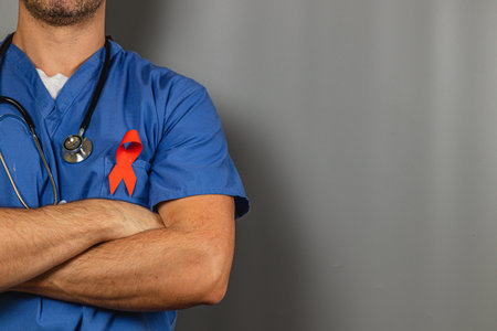 A healthcare worker stands confidently with arms crossed, wearing scrubs and a stethoscope. A red ribbon on the uniform symbolizes support for health issues and advocacy in the medical field.の写真素材