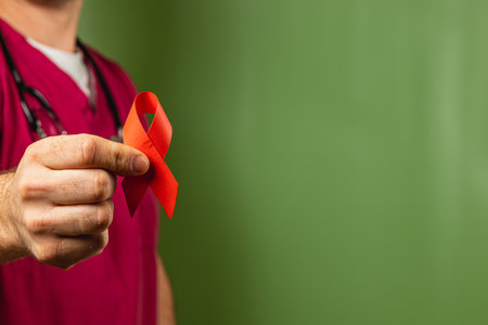 A healthcare professional holding a red ribbon against a green background, promoting awareness for important health issues. The gesture symbolizes support and advocacy in the medical community.の写真素材