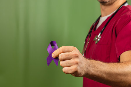 A healthcare professional in scrubs displays a purple ribbon, symbolizing awareness and support for various causes. The vibrant green background enhances the focus on the ribbon and the individual.の写真素材