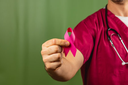 A healthcare professional in scrubs holds a pink ribbon symbolizing breast cancer awareness. This gesture is important for encouraging discussions about health and prevention efforts.の写真素材