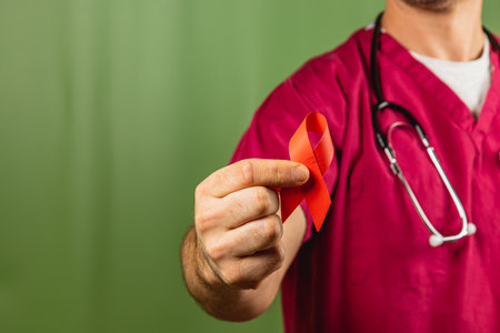 A healthcare worker wearing scrubs and a stethoscope prominently displays a red ribbon, highlighting the importance of awareness and education about various health concerns.の写真素材