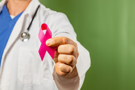 A healthcare provider in a white coat displays a pink ribbon, symbolizing support for breast cancer awareness. The focus emphasizes community health initiatives and education efforts.の写真素材