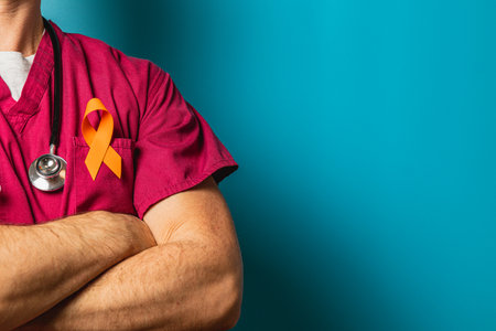 A healthcare worker stands confidently with arms crossed, wearing scrubs and a stethoscope. An orange ribbon on the uniform highlights awareness efforts related to health issues.の写真素材
