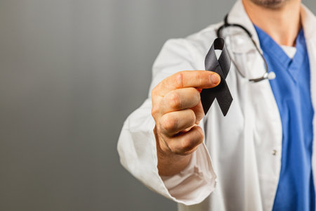 A healthcare worker in a white coat and blue scrubs holds a black ribbon, symbolizing support for various causes, in a clinical setting.の写真素材