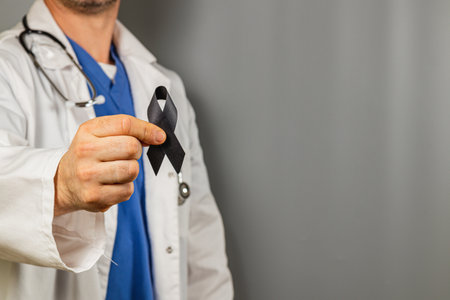 A healthcare worker stands proudly, holding a black ribbon as a symbol of support. The professional wears scrubs and a white coat, emphasizing their commitment to health awareness.の写真素材