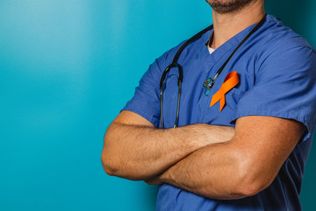 A healthcare professional stands confidently with arms crossed, wearing a blue scrubs top and a stethoscope, showcasing a vibrant orange ribbon symbolizing awareness.の写真素材