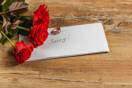 Red roses lie beside a letter that reads Sorry! and a wedding ring, symbolizing the end of a relationship. The scene conveys emotional weight and the sadness of a broken engagement.の写真素材