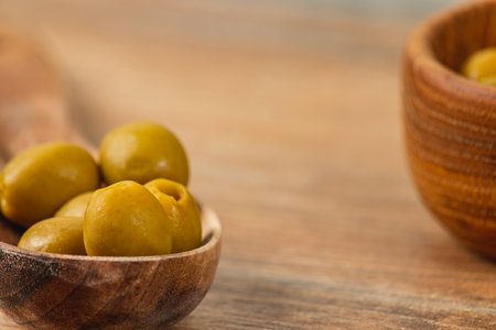 Green olives are carefully arranged in small wooden bowls, placed on a rustic wooden surface. The natural texture of the wood complements the vibrant color of the olives, creating a wholesome setting.の写真素材