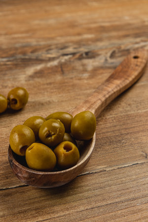 A wooden spoon holds several fresh green olives, showcasing their natural color and shape against a rustic wooden background, creating a warm, inviting atmosphere in the kitchen.の写真素材