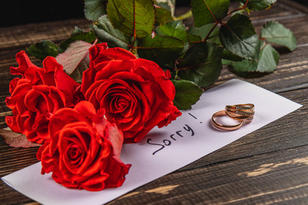 A heartfelt moment captured with vibrant red roses placed beside a note saying sorry and a broken engagement ring, symbolizing a painful separation and lost love.の写真素材